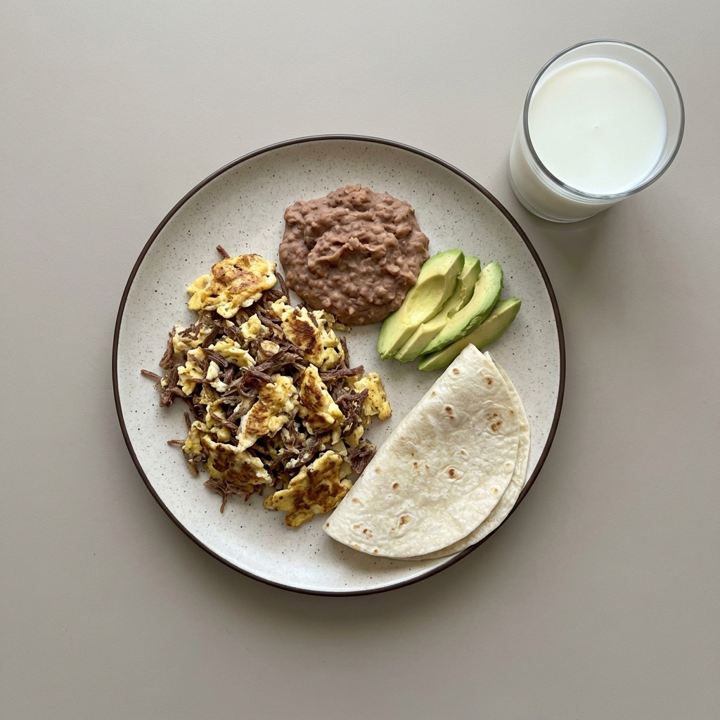 Huevos revueltos con machaca, frijoles refritos y aguacate, con vaso de leche