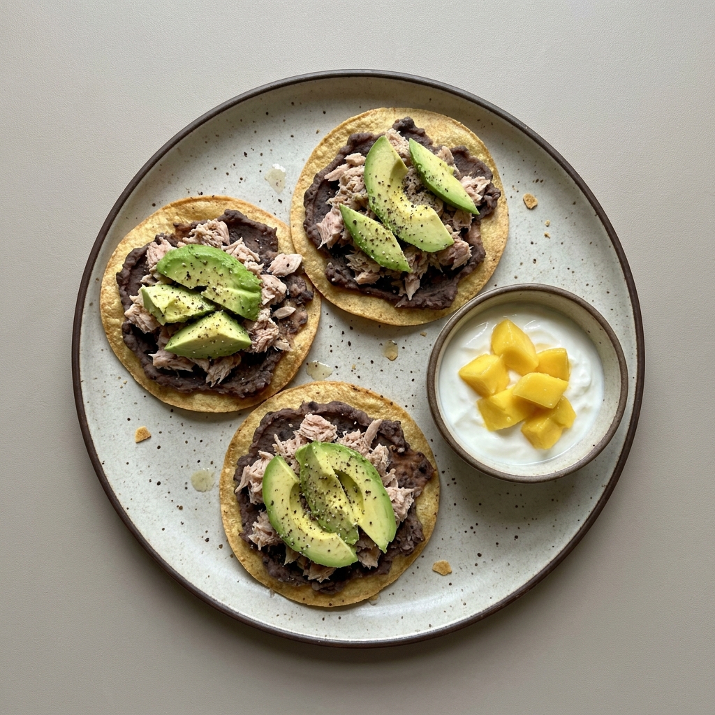 Tostadas de frijoles refritos con atún y aguacate, con bowl de yogurt griego y mango