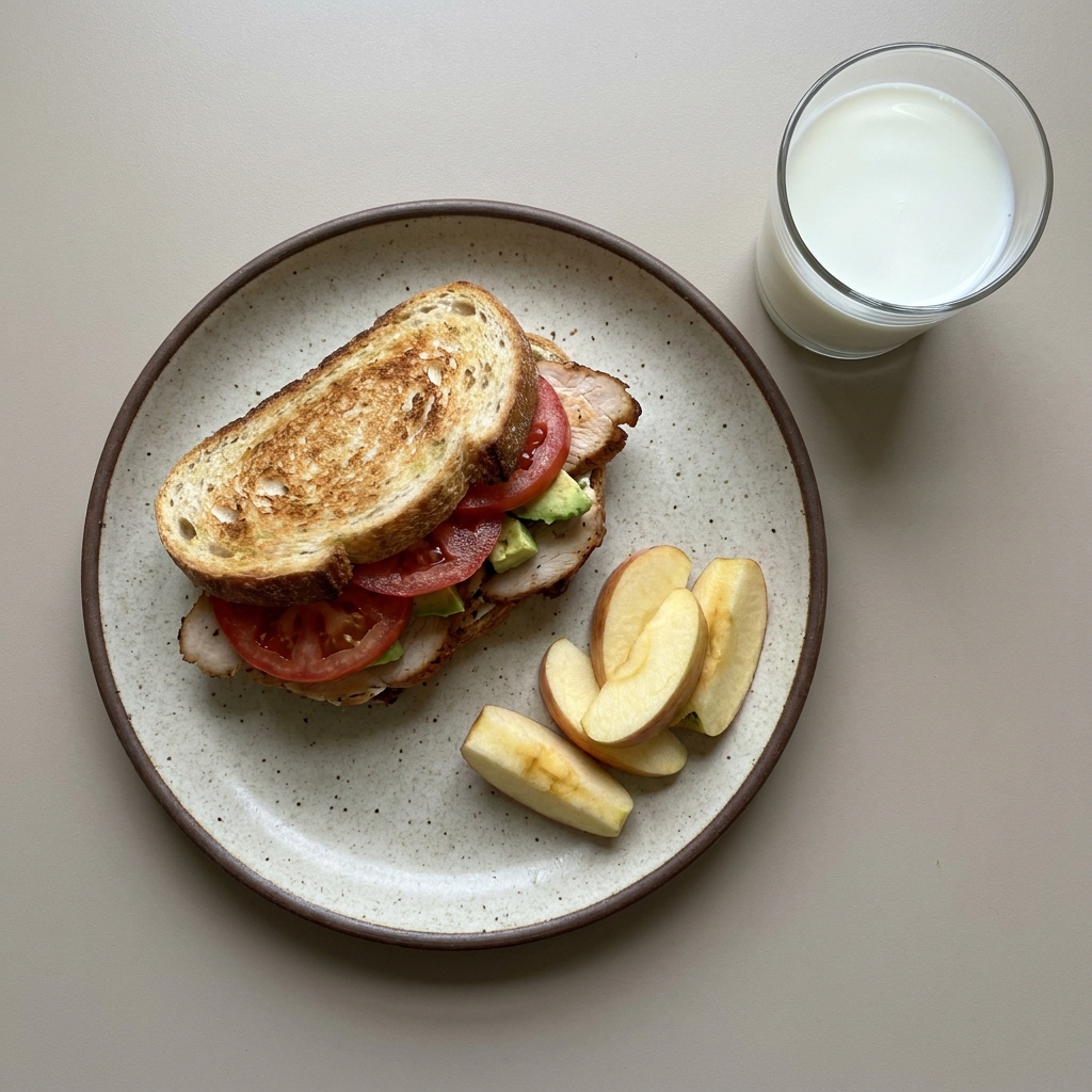 Sandwich de pavo con jitomate y aguacate, con manzana y vaso de leche