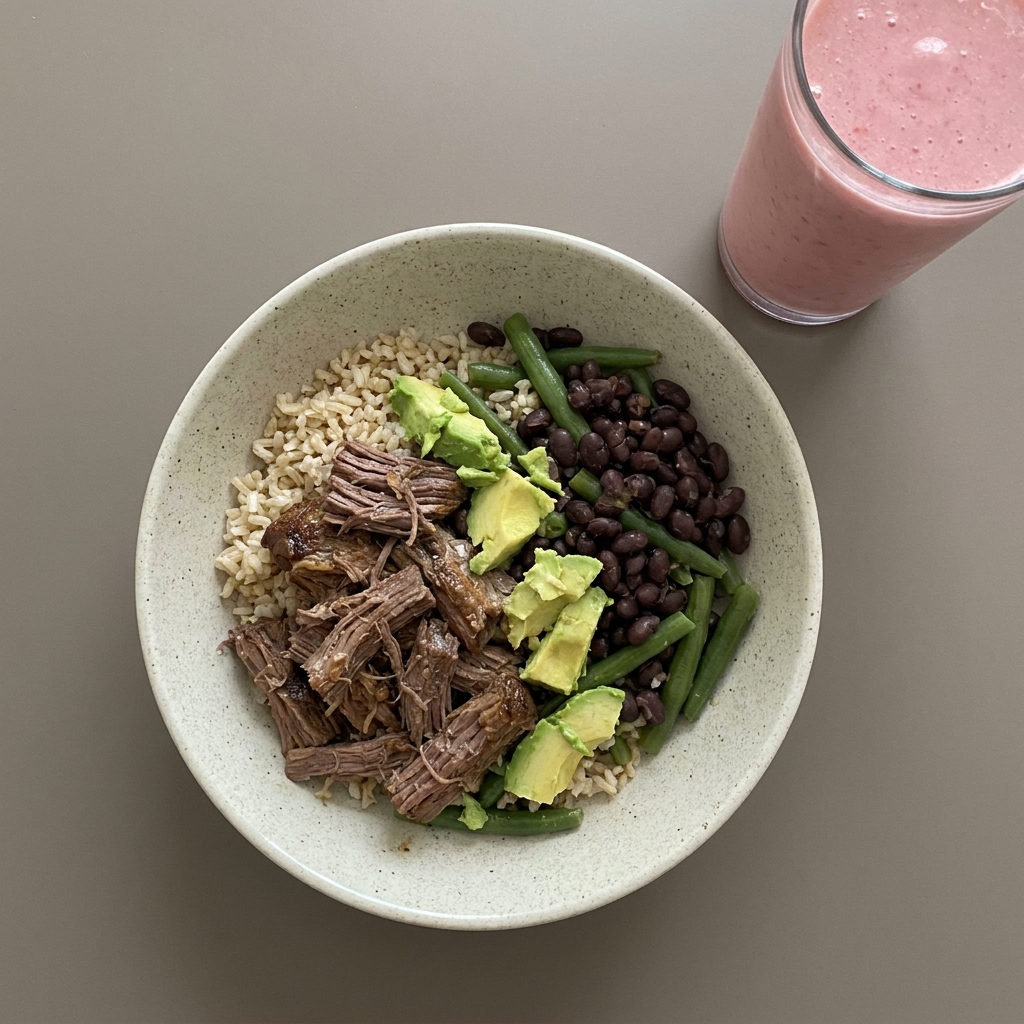Bowl de arroz integral con carne res deshebrada, frijol y ejote, con aguacate y licuado de fresa con leche